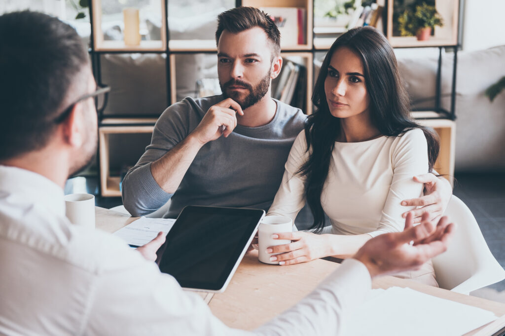 Young couple sitting at a desk discussing trust planning with their estate planning lawyer sitting on opposite of the desk. 