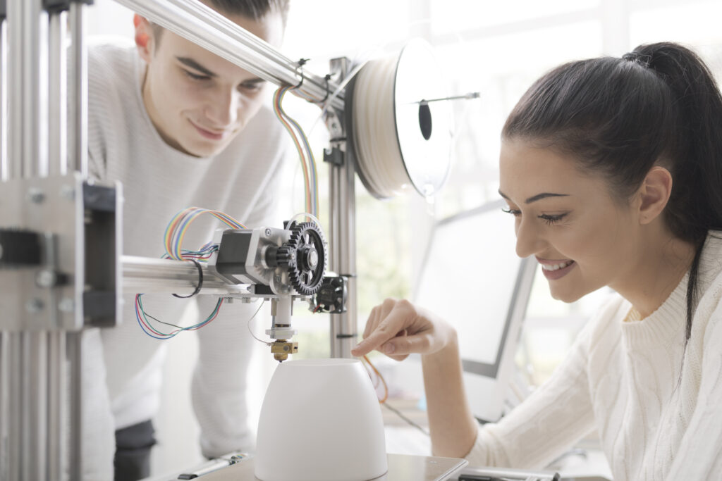 Two students in a college lab 3D printing a patentable invention to share with their patent law attorney.
