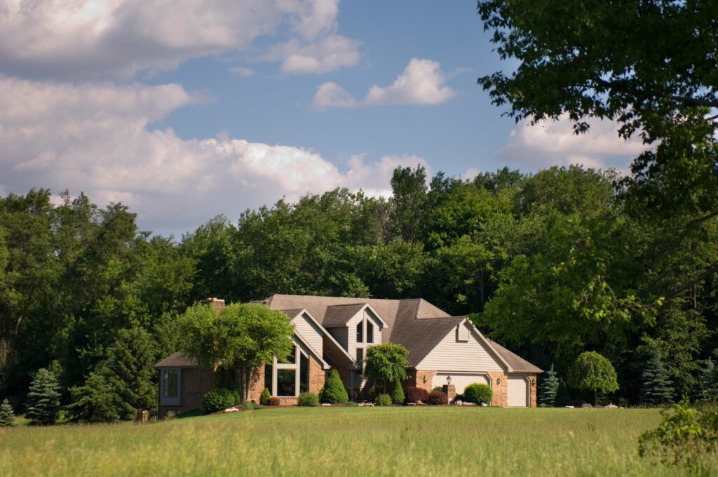 Brick house located in North West Arkansas with homestead credit, surrounded by a grassy field, with trees in the background and blue sky above. 